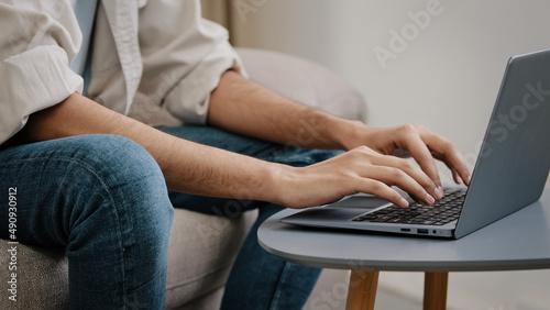 Close-up male hands typing on laptop keyboard. Unrecognizable guy unknown business man in jeans casual shirt sitting on sofa with computer working chatting e-learning email answer online distant job