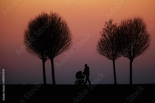 silhouette of a figure with a stroller walking along a road against a red-purple sky just after sunset