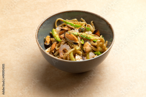 Wok with seafood and greens in a plate on a brown background.