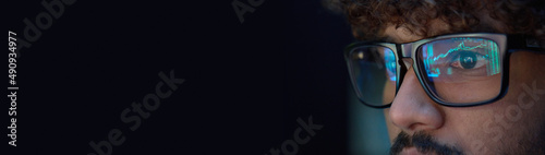 Φωτογραφία Young indian business man trader wearing glasses looking at computer screen with trading charts reflecting in eyeglasses, thinking of buying crypto, forecasting future, analyzing bank data, banner