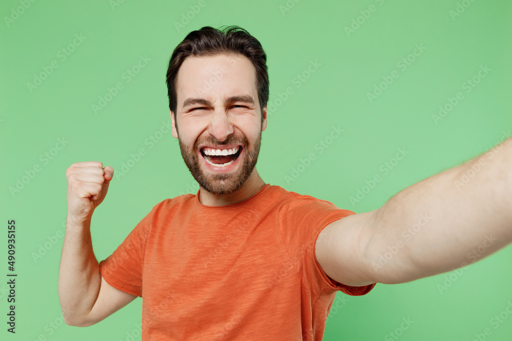 Close up young overjoyed excited happy fun man 20s wear casual orange t-shirt doing selfie shot pov on mobile phone do winner gesture isolated on plain pastel light green background studio portrait Close up young overjoyed excited happy fun man 20s wear casual orange t-shirt doing selfie shot pov on mobile phone do winner gesture isolated on plain pastel light green background studio portrait