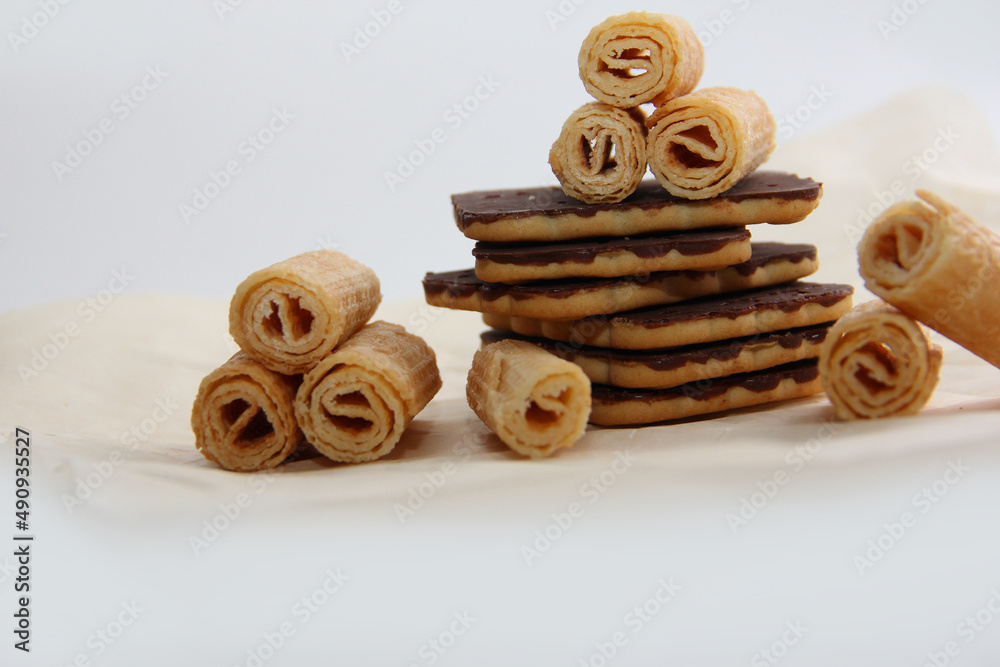 chocolate-covered cookies, waffle tubes and chocolates on parchment paper on a light background chocolate-covered cookies, waffle tubes and chocolates on parchment paper on a light background