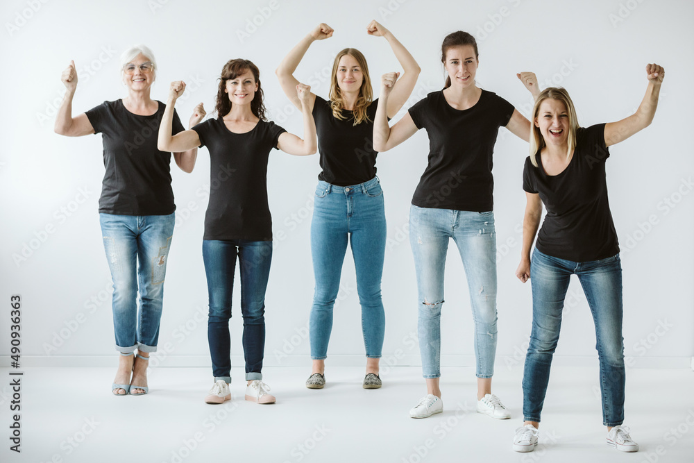 Obraz premium Five women dressed in jeans and black T-shirts raise their hands in a gesture of strength