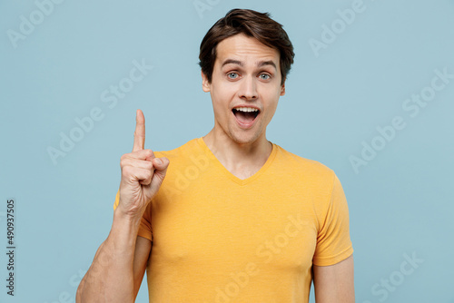 Young insighted smart proactive man 20s wear yellow blank print design t-shirt holding index finger up with great new idea look camera isolated on plain pastel light blue background studio portrait