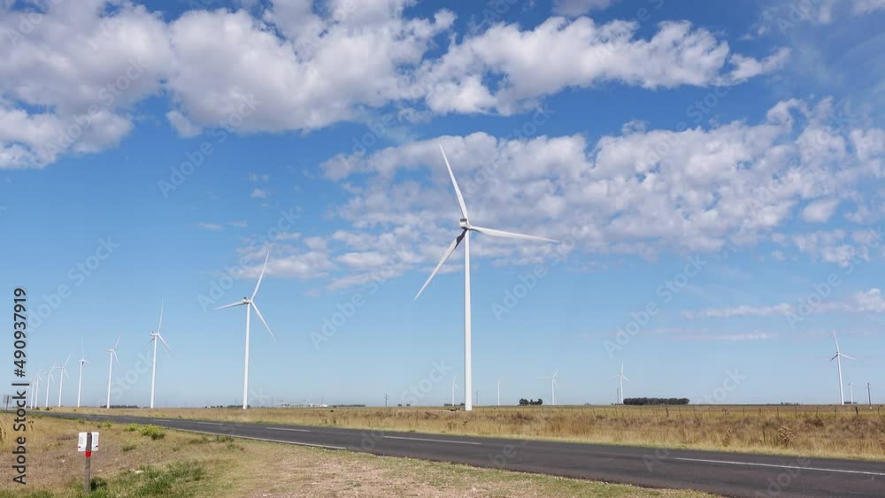 wind farm in a field next to a road. Windmills turning slowly, Blue sky with some clouds