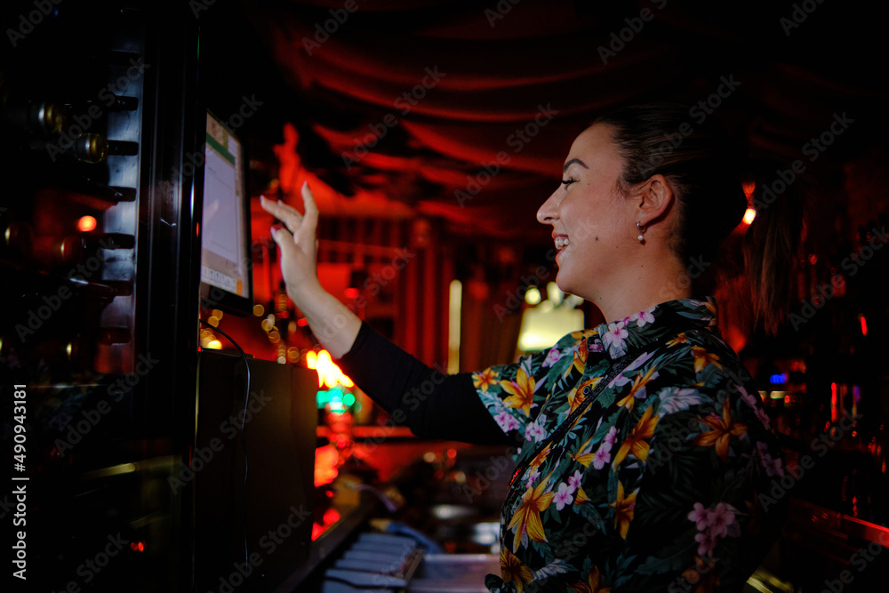 Female waitress using a touch screen computer and smiling while works behind the counter in a bar.