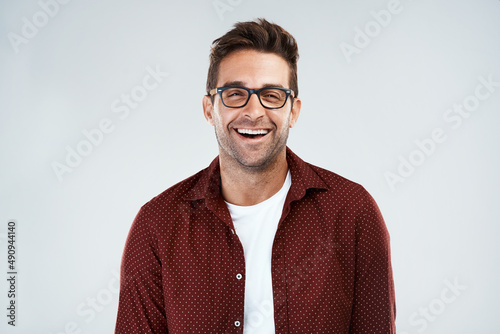 Funny and smart. Portrait of a cheerful young man wearing glasses and smiling brightly while standing against a grey background.