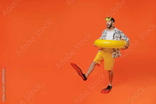 Full body side view young tourist man in beach shirt goggles hold inflatable ring flippers travel abroad on weekend isolated on plain orange background studio Summer vacation sea rest sun tan concept photo