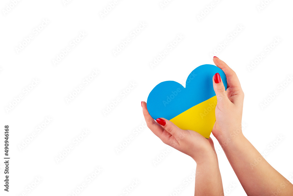 Fototapeta premium The hand of a young Ukrainian girl holds a heart of a yellow-blue flag on isolated white background. The concept of participation of the Ukrainian people in the war with Russia. Not war concept