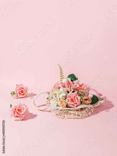 Floral arrangement with fresh flowers and crochet bag on pastel pink background. Creative Spring holiday bloom concept. Minimal festive romantic floral arrangement. Florist shop idea with copy space.