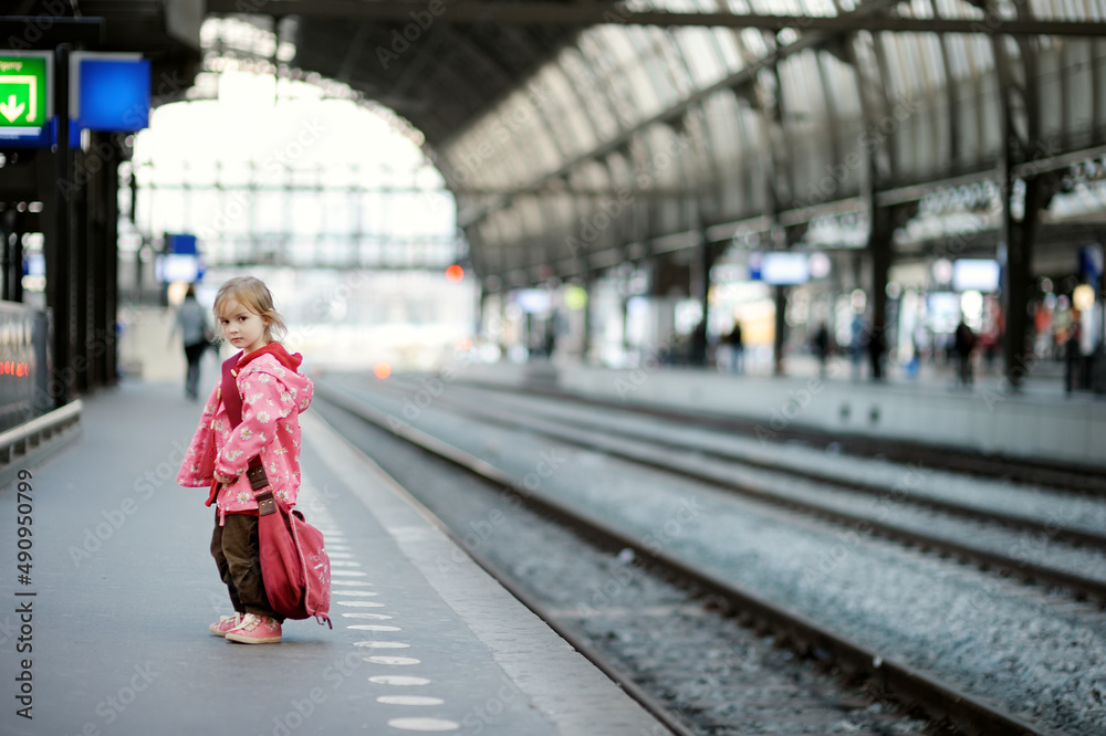 Cute little girl with big shoulder bag standing on a railway station. Kid waiting for a train.