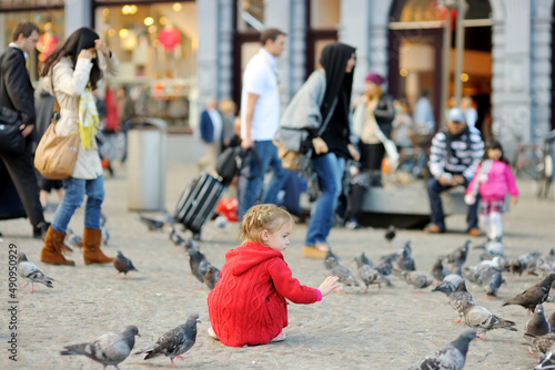 Cute little girl feeding and chasing birds on Dam Square in Amsterdam on summer day.