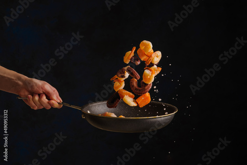 Seafood. Professional chef prepares pieces of red fish and octopus in a pan on a black background. Levitation. Useful diet food. Restaurant, hotel, advertising, banner.