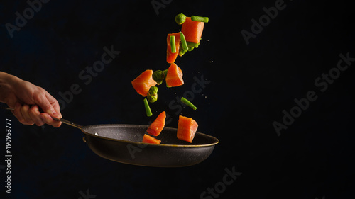 Sea food. Pieces of red fish - salmon, trout with vegetables in a frying pan in a frozen flight on a black background. Healthy vegetarian food. Restaurant, hotel, banner.