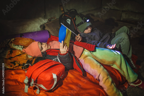 Thoughtful little kids with Ukrainian flag lay in a bomb shelter and waits for the end of the air attack of Russian invaders, terrorism and war, current history photo