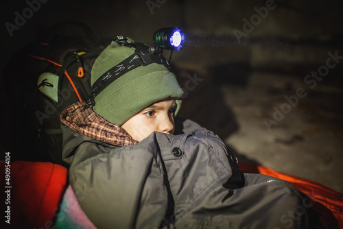 Thoughtful little boy with headlamp lays in a bomb shelter and waits for the end of the air attack of Russian invaders, terrorism and war, current history photo