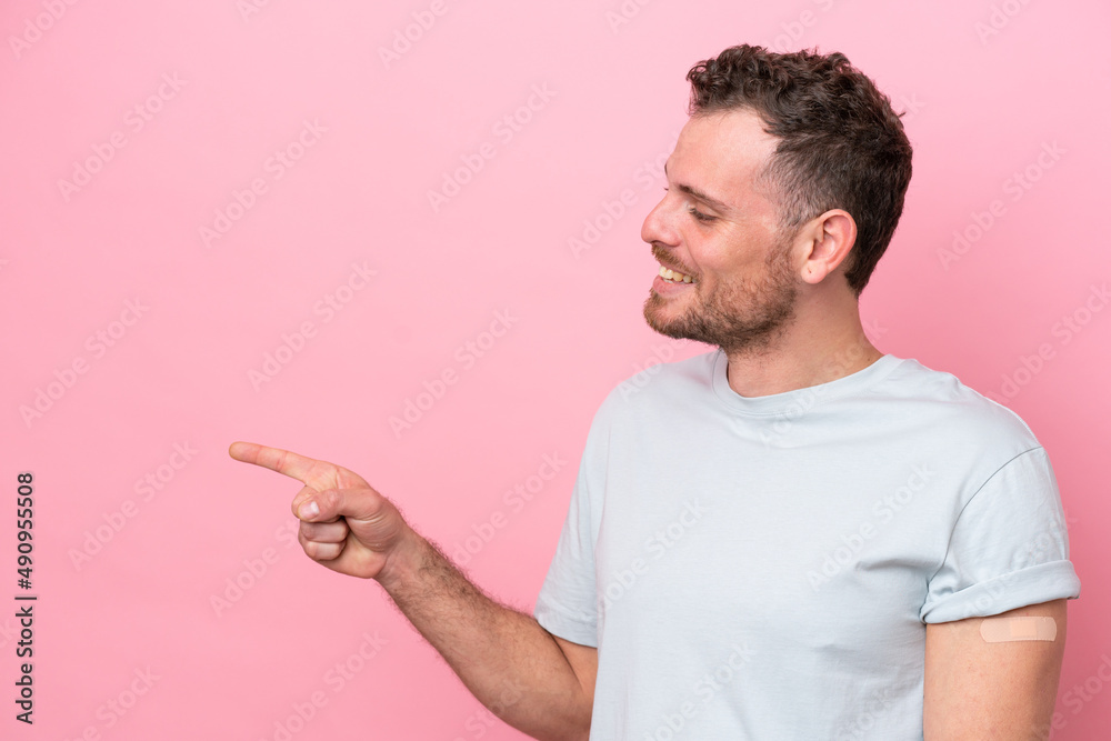 Young Brazilian man wearing a band-aids isolated on pink background pointing to the side to present a product Young Brazilian man wearing a band-aids isolated on pink background pointing to the side to present a product