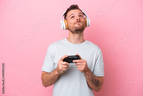 Young Brazilian man playing with video game controller isolated on pink background and looking up © luismolinero