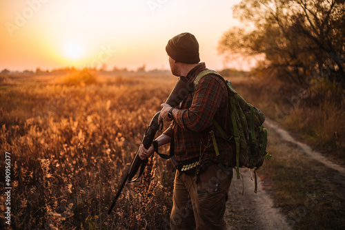 Young strong soldier with riffle and ammunition belt moving outdoors by the dirt road in sunset time