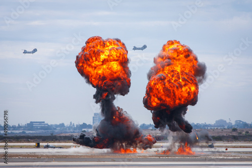 Bomb explosion at an airfield with combat helicopters in the background