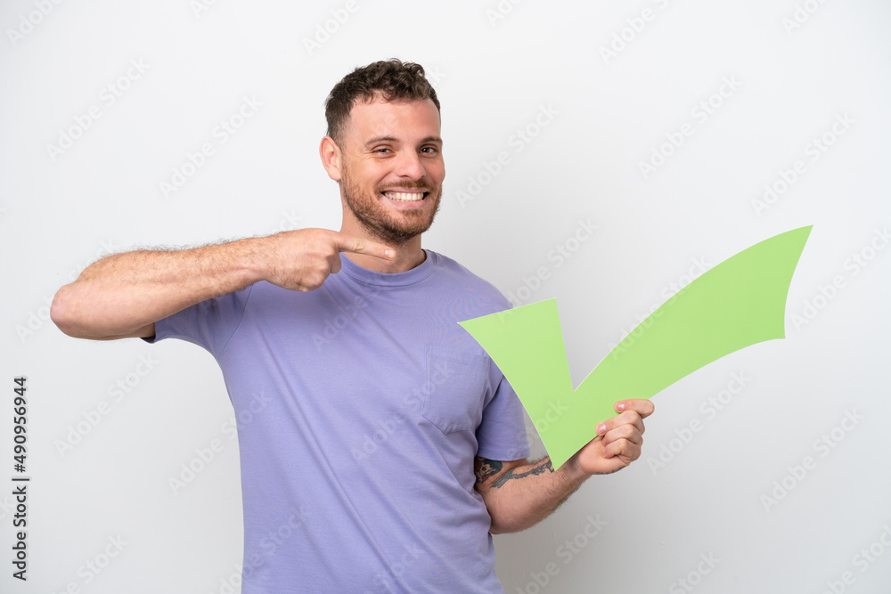 Young Brazilian man isolated on white background holding a check icon and pointing it Young Brazilian man isolated on white background holding a check icon and pointing it