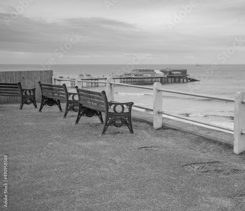Black and white photo of the wooden benches on Cromer clifftop over looking the beach and famous Victorian era pier.