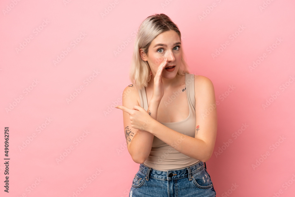 Young caucasian woman isolated on pink background pointing to the side to present a product and whispering something Young caucasian woman isolated on pink background pointing to the side to present a product and whispering something