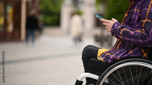 Woman with disability who uses a wheelchair using a smartphone while out in the city photo