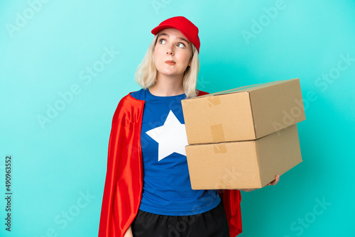 Super Hero caucasian delivery woman isolated on blue background and looking up