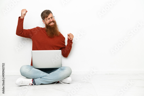 Young reddish caucasian man with laptop isolated on white background celebrating a victory © luismolinero