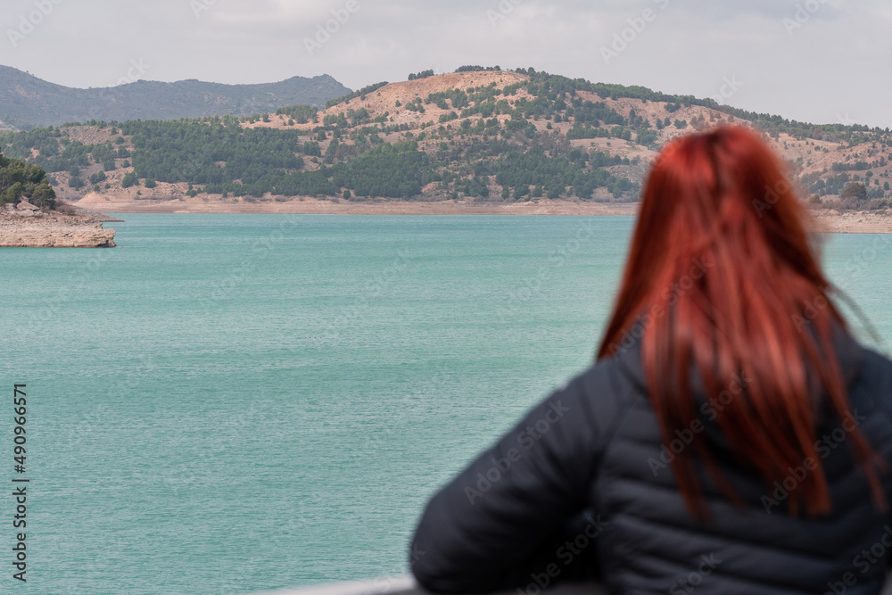 unrecognisable red-haired woman observes reservoir with turquoise water