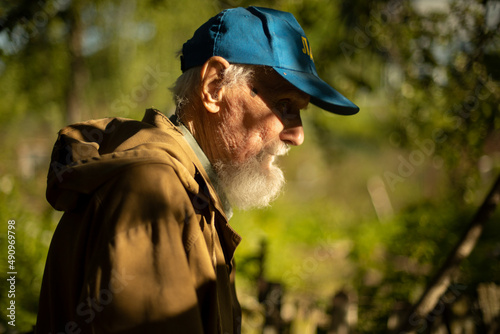 An old man with a gray beard in Russia. A pensioner in the garden in a blue cap. Portrait in profile of a Russian man.