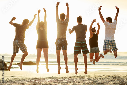 Catching air at the beach. Rearview shot of a group of unidentifiable friends jumping together on the beach at sunset.