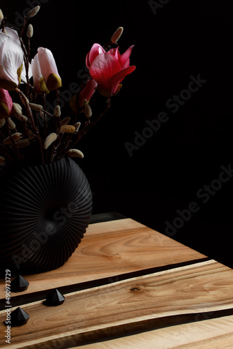 Expensive vintage furniture. The table is covered with epoxy resin and varnished. Luxury quality wood processing. A bouquet of red and pink flowers in a minimalistic black flowerpot.