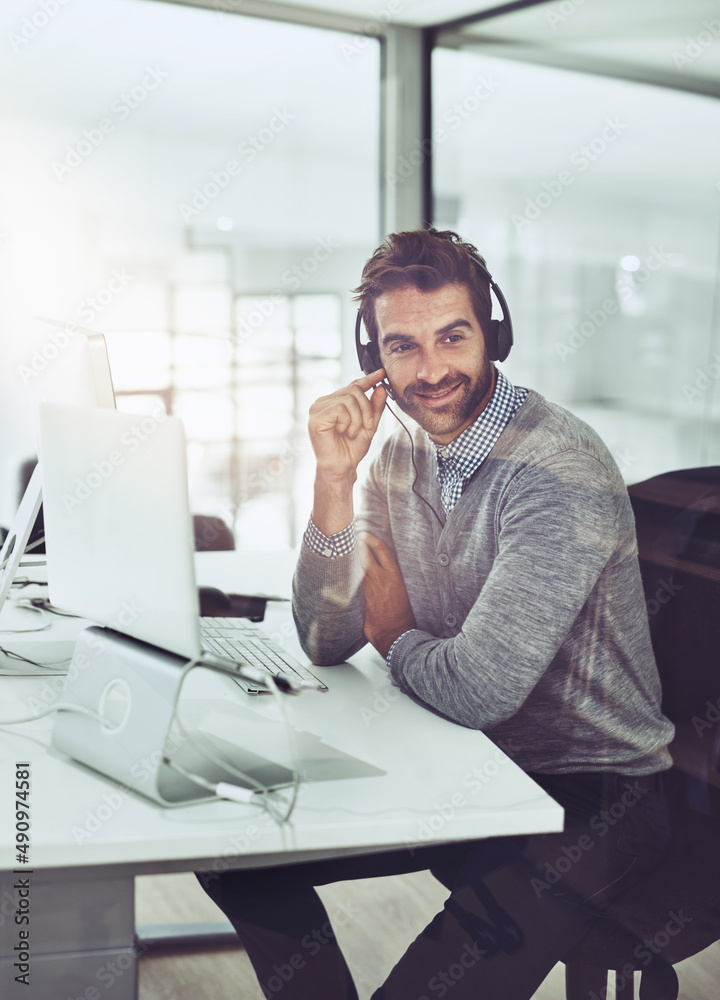 Service with a smile. High angle shot of a handsome young businessman wearing a headset while sitting at his desk.