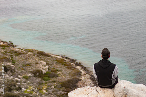 Back view of young man sitting on rocks on cliff. Happiness, travel alone and freedom concept.