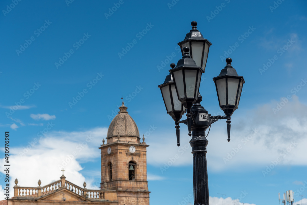 Old street lamp with bell tower of the church in the city Tunja. Colombia.
