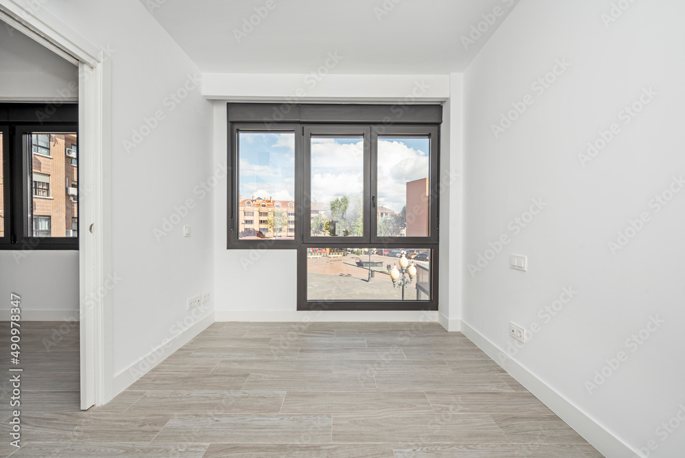 Fototapeta premium Empty living room with wood-like stoneware floors, large windows overlooking a square