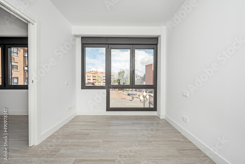 Empty living room with wood-like stoneware floors, large windows overlooking a square