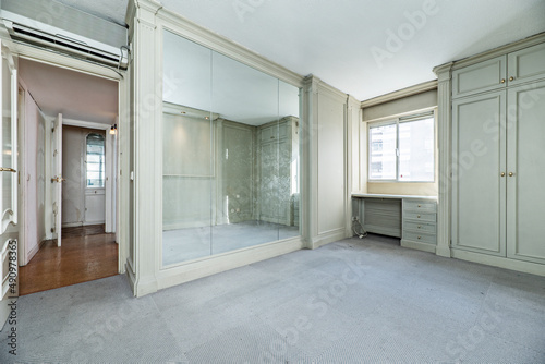 empty room with walls covered with wooden mural with cabinets and mirrors and floors covered with gray carpet