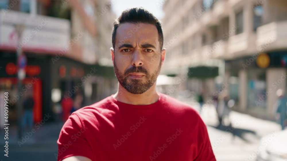 Young hispanic man smiling confident doing obscene gesture with finger at street