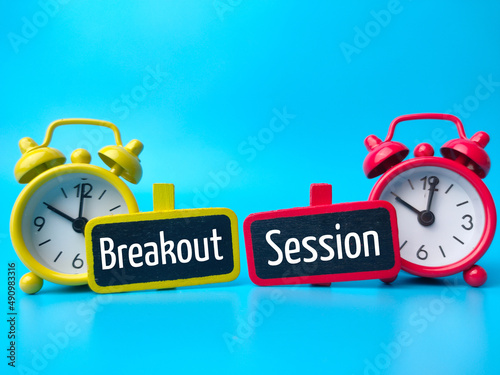 Alarm clock and wooden board with text Breakout Session on blue background.