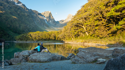 A couple sitting on the rocks and enjoying the views of Lake Mackenzie at Routeburn Track at sunset. Moon rising above the mountains. South Island. photo