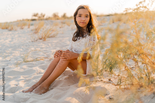  Summer photo of small girl in stylish boho outfit posing on the beach. Warm sunset colors. Wacation and  travel concept. photo