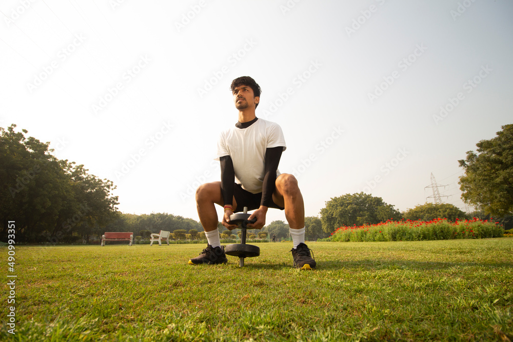 Young Indian boy working out with a dumble in park early in the morning. Healthy lifestyle and motivation concept. Young Indian boy working out with a dumble in park early in the morning. Healthy lifestyle and motivation concept.