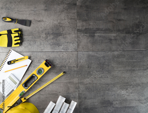 Contractor theme. Tool kit of the contractor: yellow hardhat, libella, hand saw. Plans and notebook on the gray tiles.