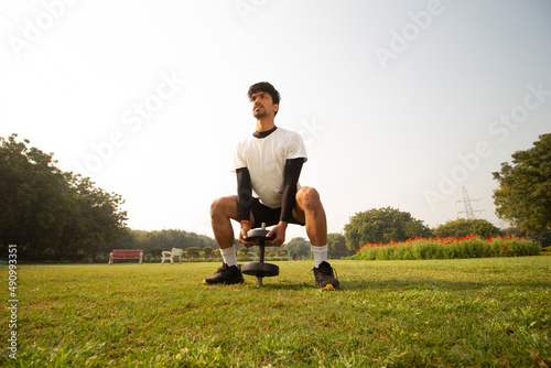 Young Indian boy working out with a dumble in park early in the morning. Healthy lifestyle and motivation concept. photo
