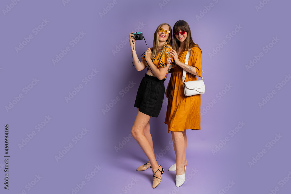 Two pretty women , best friends, posing on purple background in trendy summer outfit. Full lenght. Two pretty women , best friends, posing on purple background in trendy summer outfit. Full lenght.