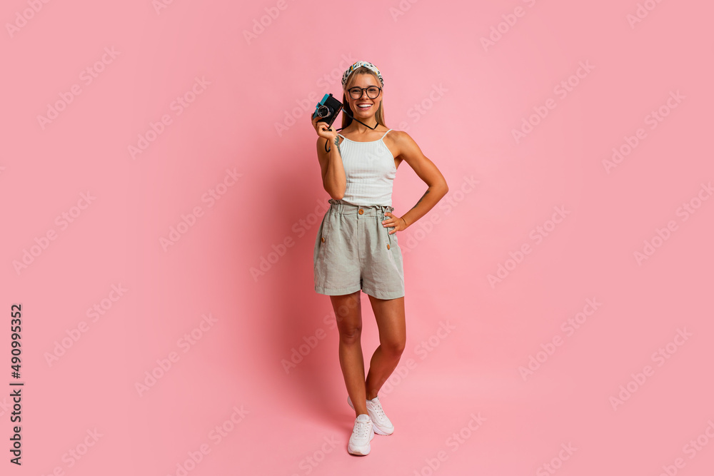 Laughing blond woman holding retro camera and posing on pink background. Travel and summer vacation concept. Full lenght. Laughing blond woman holding retro camera and posing on pink background. Travel and summer vacation concept. Full lenght.