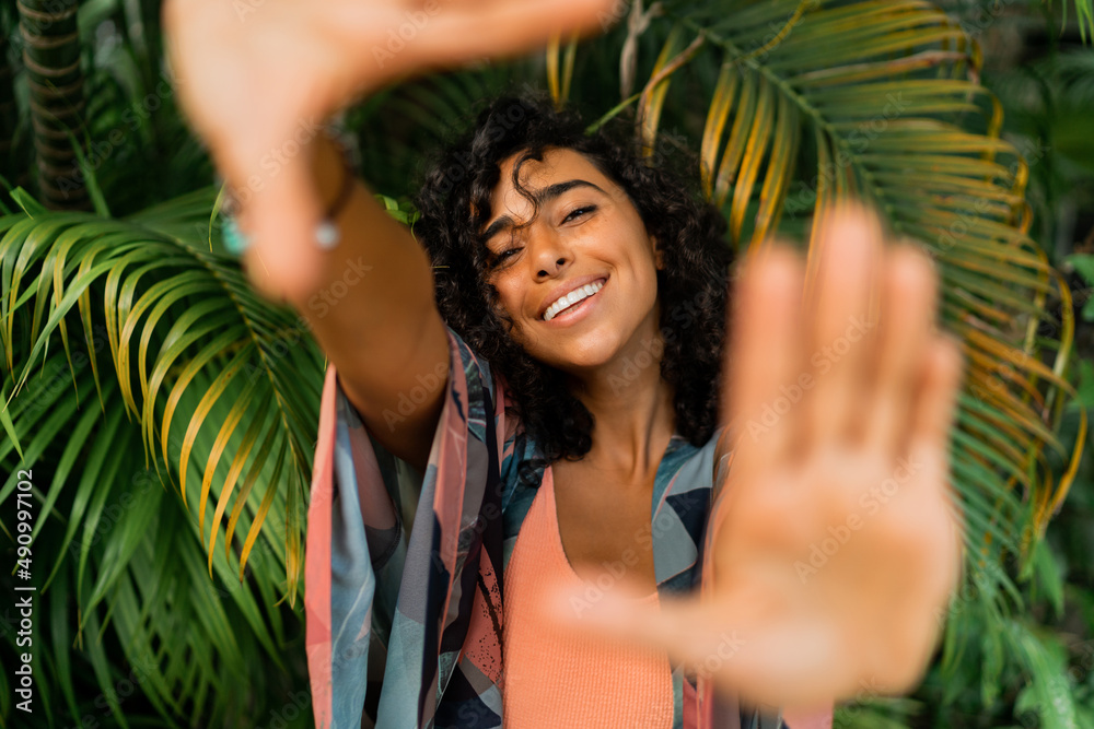 Outdoor portrait of blissful lovely woman with curly hairs posing over tropical trees and palm leaves. Outdoor portrait of blissful lovely woman with curly hairs posing over tropical trees and palm leaves.